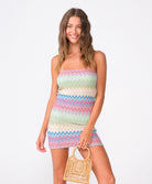 A woman wearing  a colorful striped mini dress standing against a white wall. 