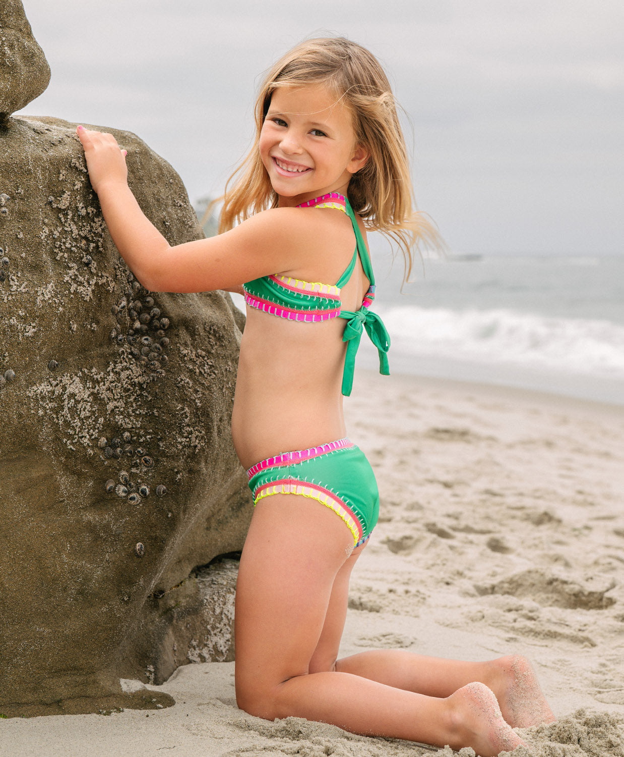 Young girl in a colorful bikini sitting on a beach.