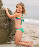 Young girl in a colorful bikini sitting on a beach.