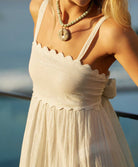 A woman wearing a white dress standing outside on a patio.