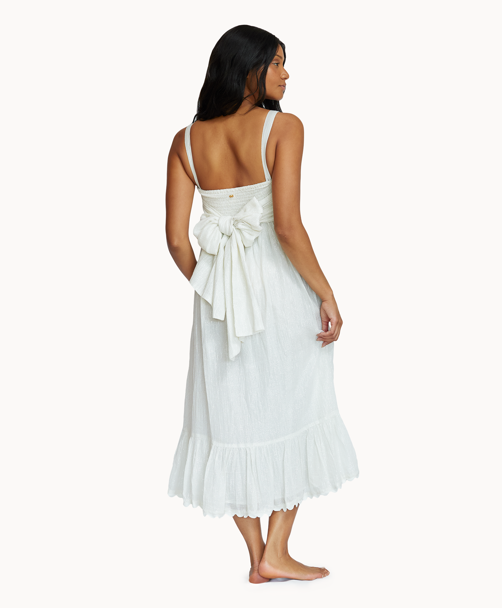 A woman wearing a midi length white dress acing towards a white wall. 