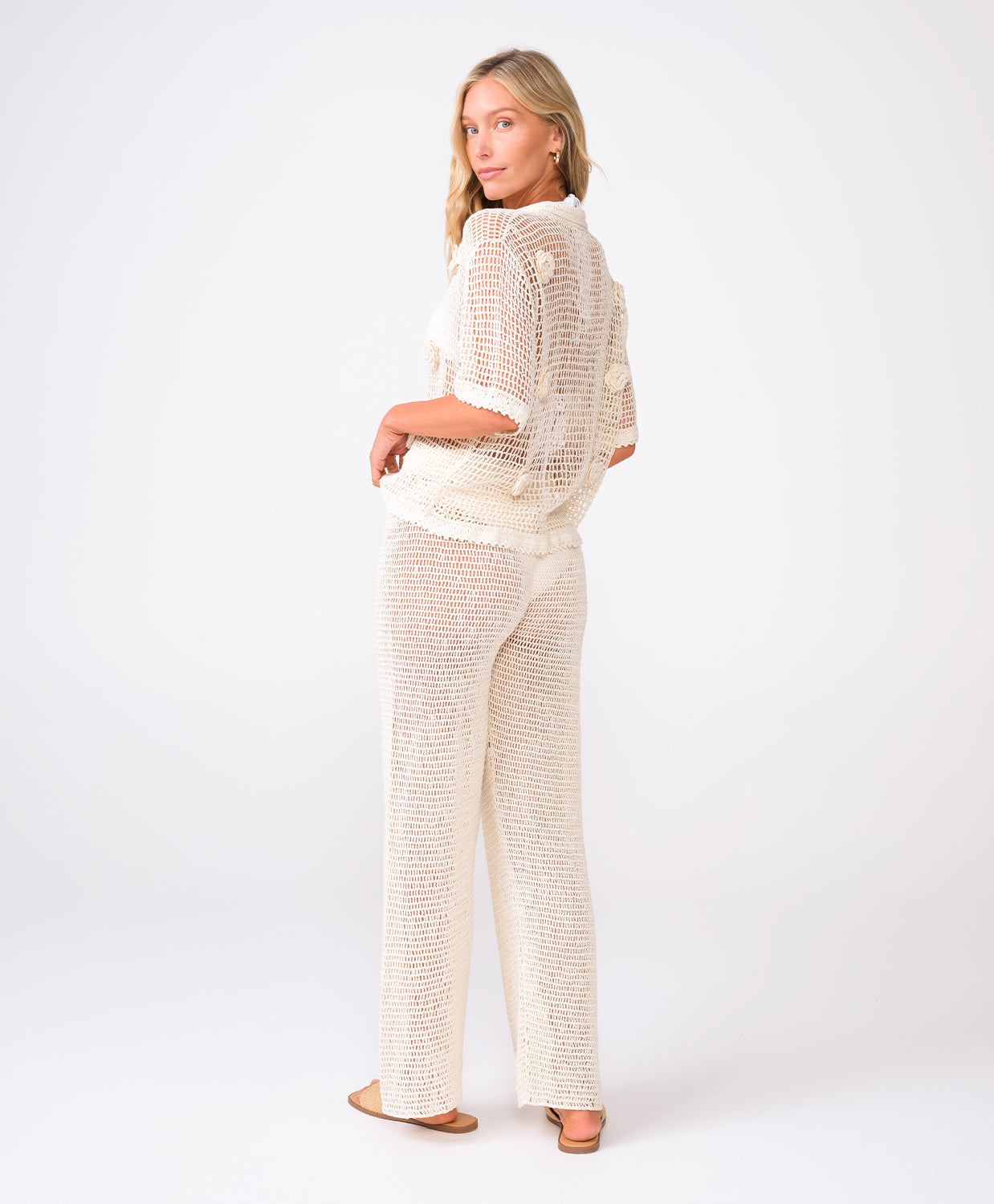 A woman wearing an ivory knit shirt and matching pants standing against a white wall.