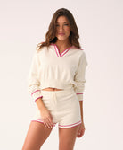 Woman wearing a white sweater and shorts with pink trim on a plain background