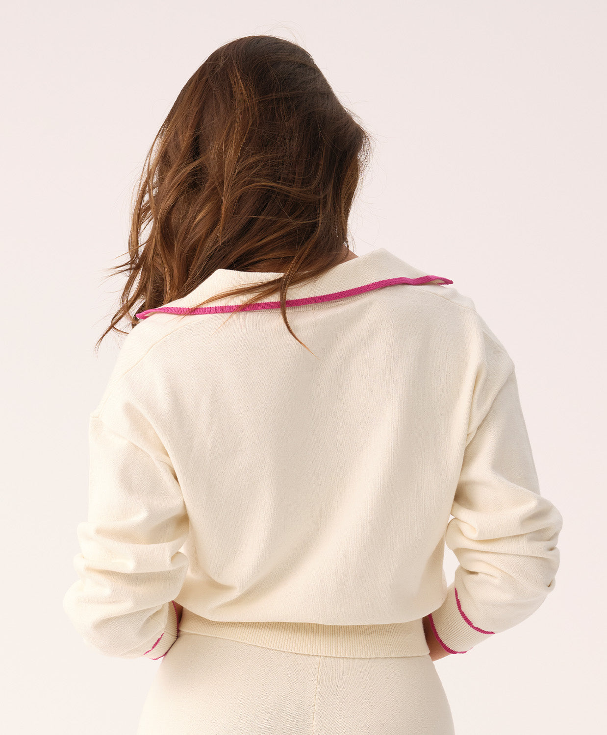 Woman wearing a white sweater and shorts with pink trim on a plain background