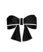 A black bikini top with a large bow against a white wall. 