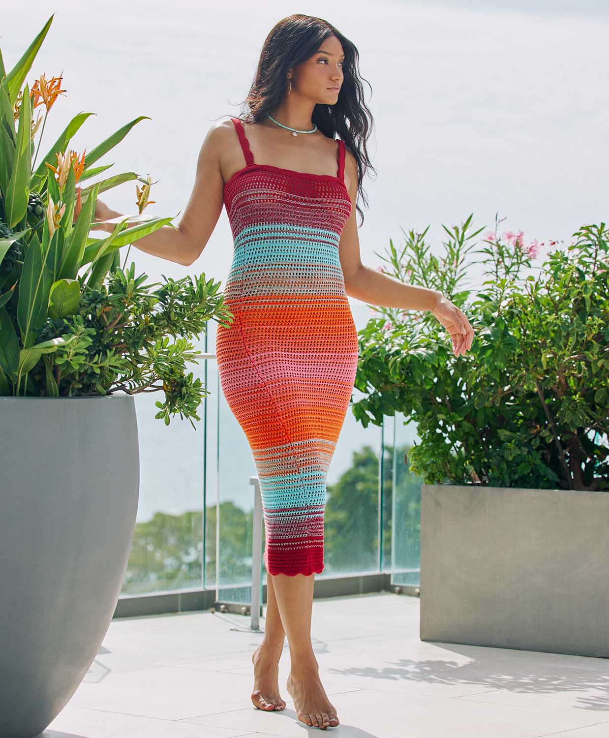 A woman wearing a midi length knit dress standing outside new flowers. 