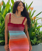 A woman wearing a knit dress sitting against a pot of flowers.