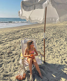 A young girl wearing a pink and orange bikini sitting on a chair under an umbrella.