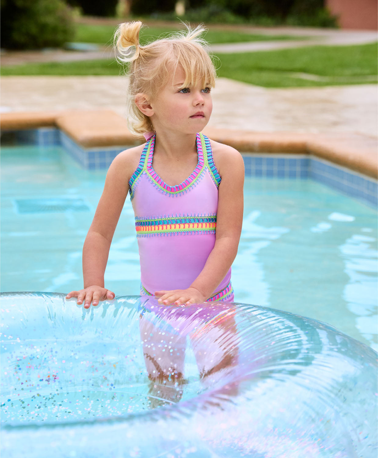 A blonde girl wearing a pink tankini swimsuit playing in the pool with a blow up inner tube.