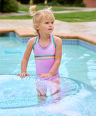 A blonde girl wearing a pink tankini swimsuit playing in the pool with a blow up inner tube.