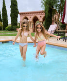 A brunette girl wearing a colorful bikini and another brunette girl wearing a colorful one piece. Both girls are standing in a pool. 