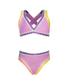 A pink bikini with colorful embroidered trim against a white wall.