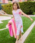 A brunette girl wearing a white lace cover up dress walking on grass.