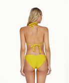 Blonde woman wearing a yellow bikini facing towards a white wall.