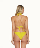 Blonde woman wearing a yellow bikini facing towards a white wall.