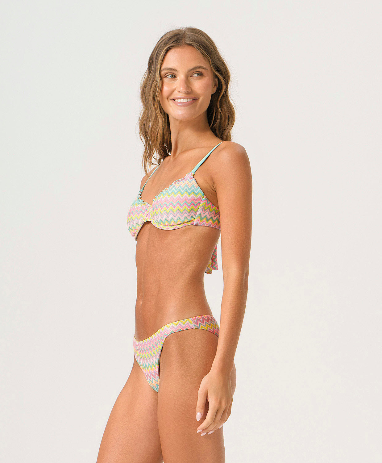 Woman wearing a striped bikini with a zig zag pattern against a white wall.