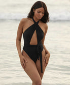 A woman wearing a black halter style one piece standing in the ocean.