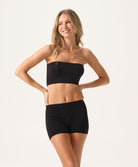 A woman wearing a black bandeau and matching shorts standing against a white wall.