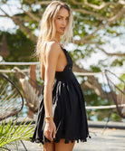 A blonde woman wearing a short black dress standing in front of palm leaves outside. 