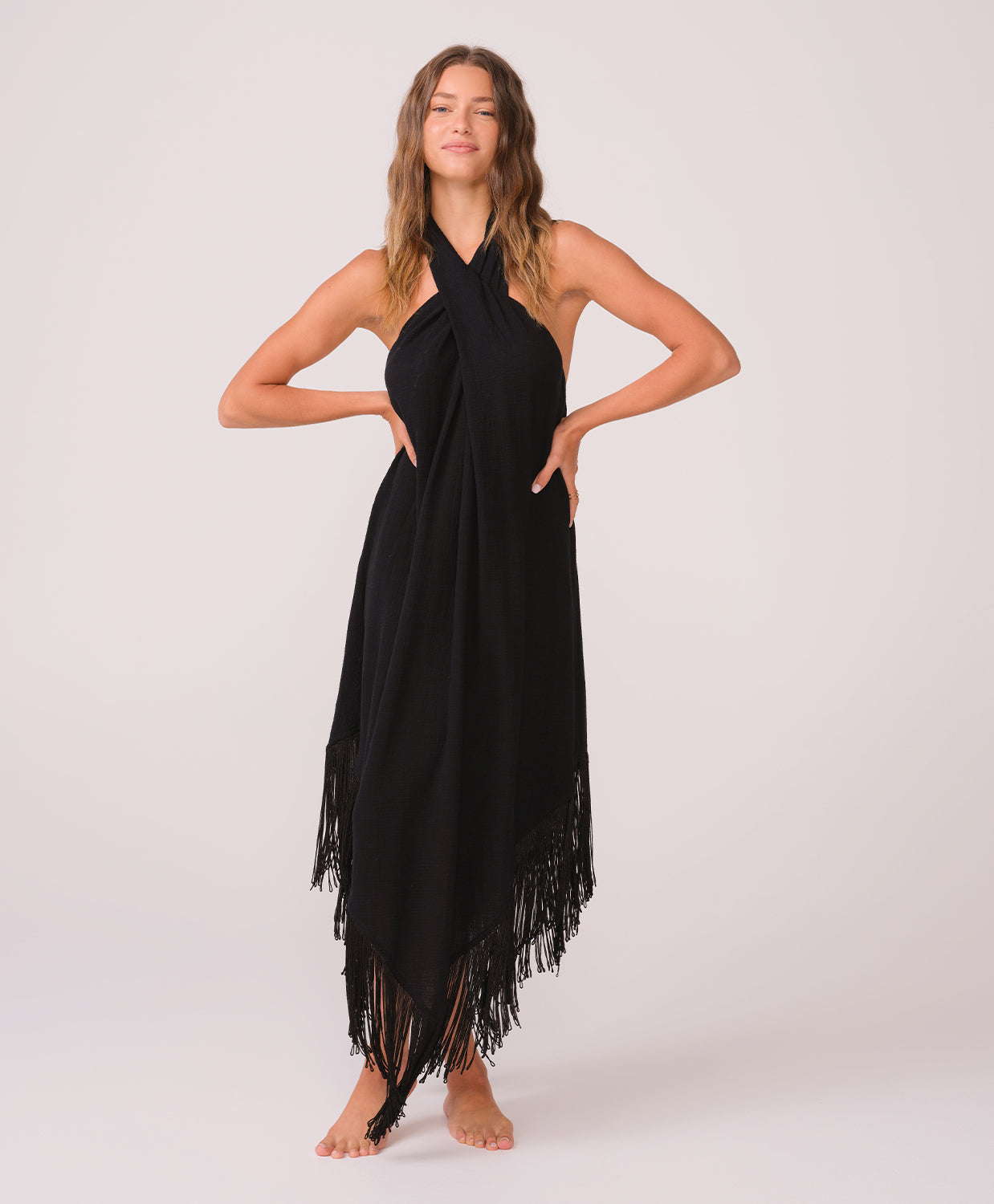 Woman wearing a black long fringe dress standing against a white wall.