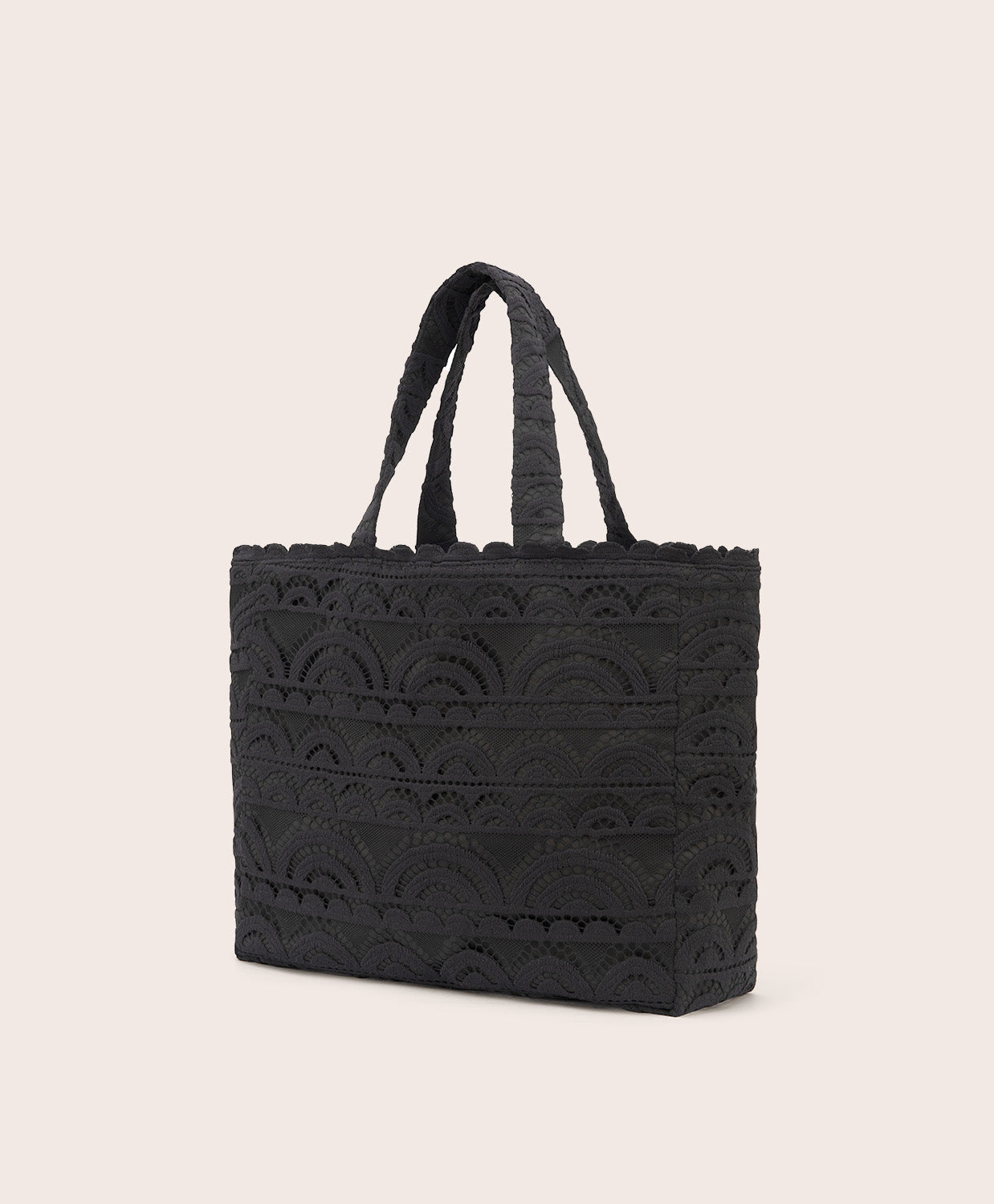 A black lace tote with scalloped trim against a white wall 