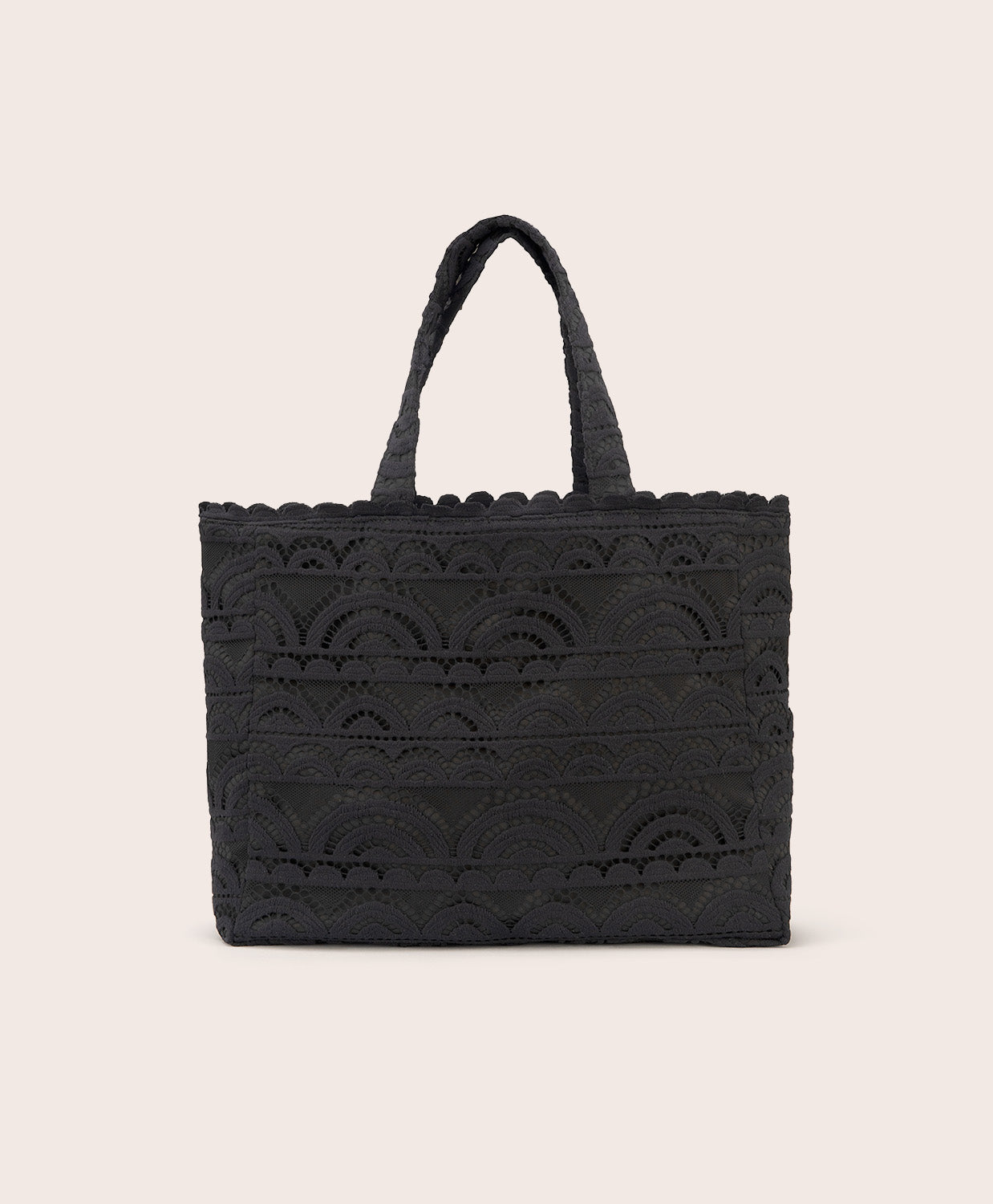 A black lace tote with scalloped trim against a white wall 