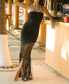 Woman wearing a black fringe dress standing by a poolside.