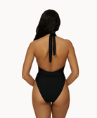 Back view of woman wearing a black one piece in front of a white background. 