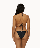Back view of woman wearing a black lace bikini in front of a white background. 