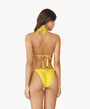 Brunette woman wearing a yellow macrame triangle shape bikini facing backwards towards a white wall.