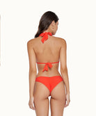 Back view of brunette woman wearing a neon orange bikini in front of a white background. 