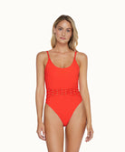 Blonde woman wearing a neon orange beaded one piece in front of a white background. 