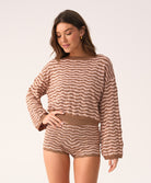 A woman wearing a long sleeve brown and beige striped top and matching shorts standing in front of a white wall.