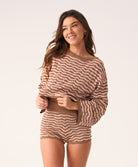 A woman wearing a long sleeve brown and beige striped top and matching shorts standing in front of a white wall.