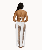 Back view of woman wearing white sarong in front of a white background. 