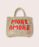 A purse/tote that says "More Amore" in pink letters against a white wall.