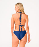 Back view of blonde woman wearing a navy blue bikini in front of a white background. 