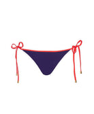 A navy bikini bottom with red tie sides against a white wall.