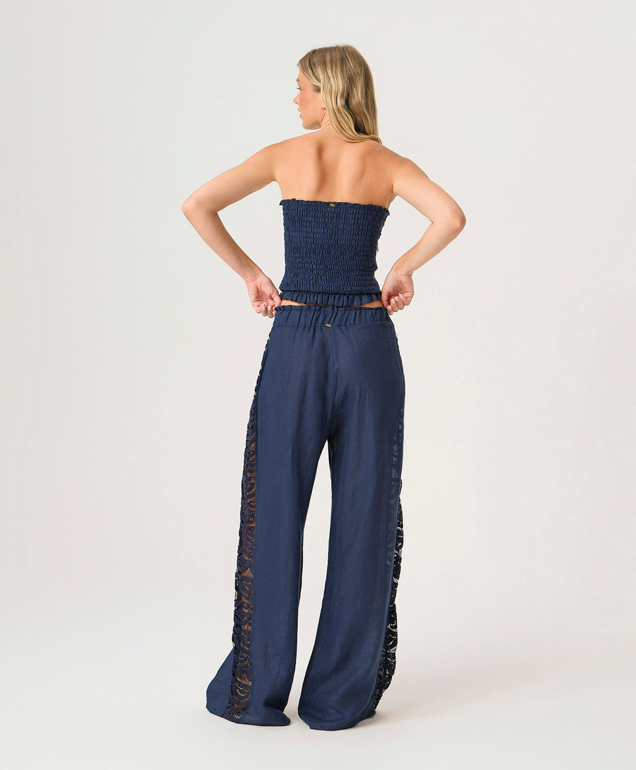 Woman wearing a navy strapless top and wide-leg pants with lace details on a white background