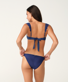 A woman shown from the back wearing a navy blue bikini against a plain light background.