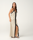 A woman modeling a long cream linen maxi dress with black trim and a black front placket, photographed against a seamless white studio background.