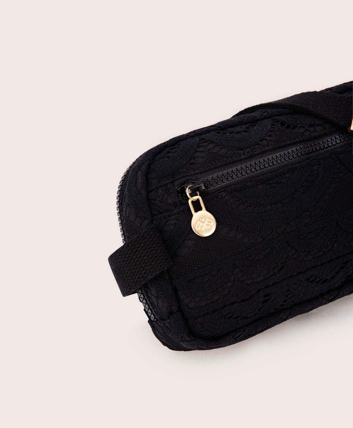 A black lace crossbody bag against a white wall. 