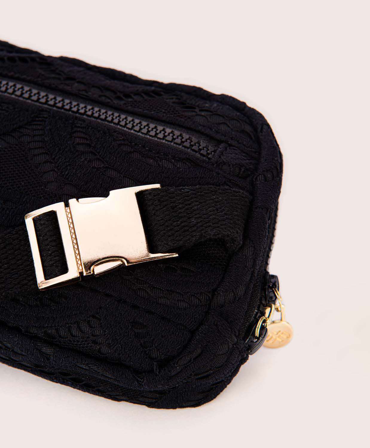 A black lace crossbody bag against a white wall. 