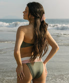 Woman in a green bikini standing on a beach with ocean waves in the background