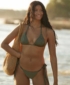 A woman wearing a green triangle top bikini standing on the beach near the ocean. 