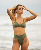 A woman wearing a green bikini standing on the beach near the ocean. 