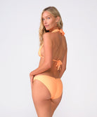 A woman wearing an orange bikini standing against a white wall.