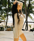 Woman in a beige dress standing by a pool with palm trees in the background