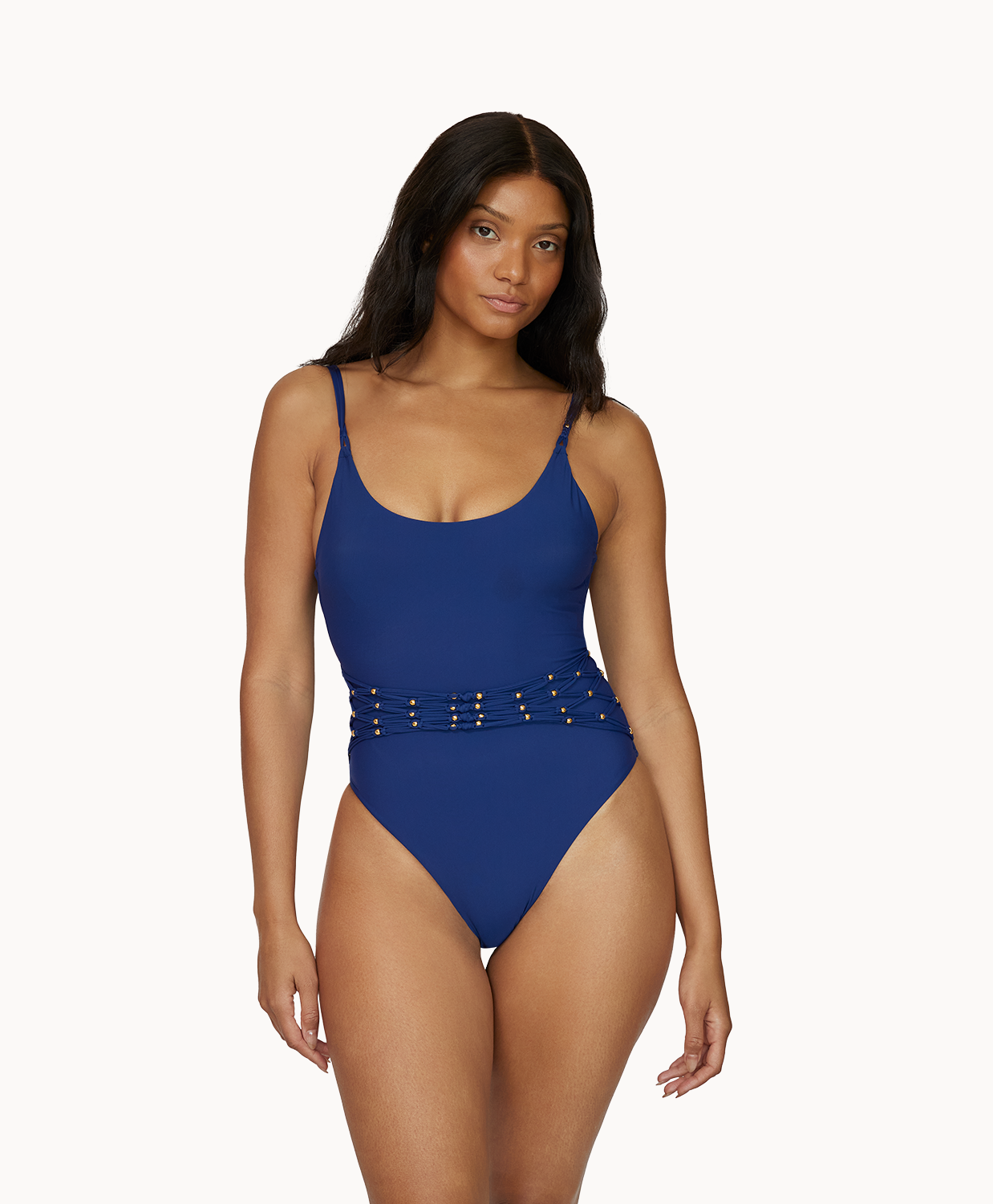 A woman wearing a navy one piece swimsuit standing against a white wall. 