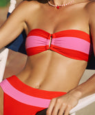 A woman wearing a pink and red striped bandeau bikini sitting on a white chair outside.